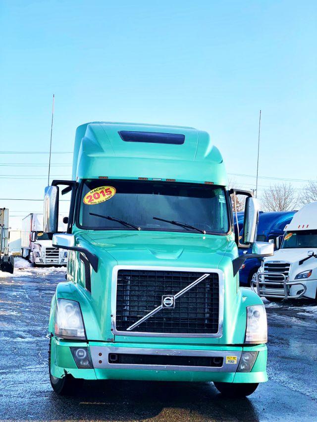 2015 Volvo VNL 670 front view, turquoise truck with large grille, Volvo emblem, windshield wipers, and sticker on windshield.