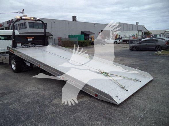 Flatbed tow truck bed with hydraulic tilt in a parking lot; Freightliner branding not visible in this image.