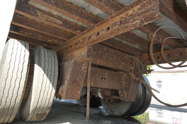 Trailer underside showing rusted frame, dual rear wheels, and suspension components.