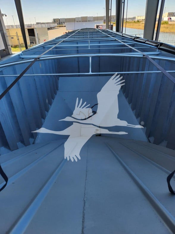 Trailer interior showing long blue hopper trailer with vertical ribs and a pale blue floor; top rails and crossbars visible along sides; watermark of a flying bird logo centered.