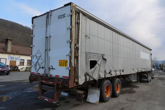 Curtainside trailer with tri-axle bottom rear view showing damaged tarp and weathered exterior panels.