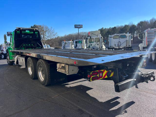Flatbed rollback truck with extended platform and dual rear axles in a dealership lot.
