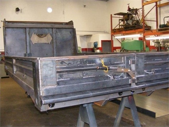 Dump bed truck body showing metal construction, with side panels and tailgate, in a workshop.