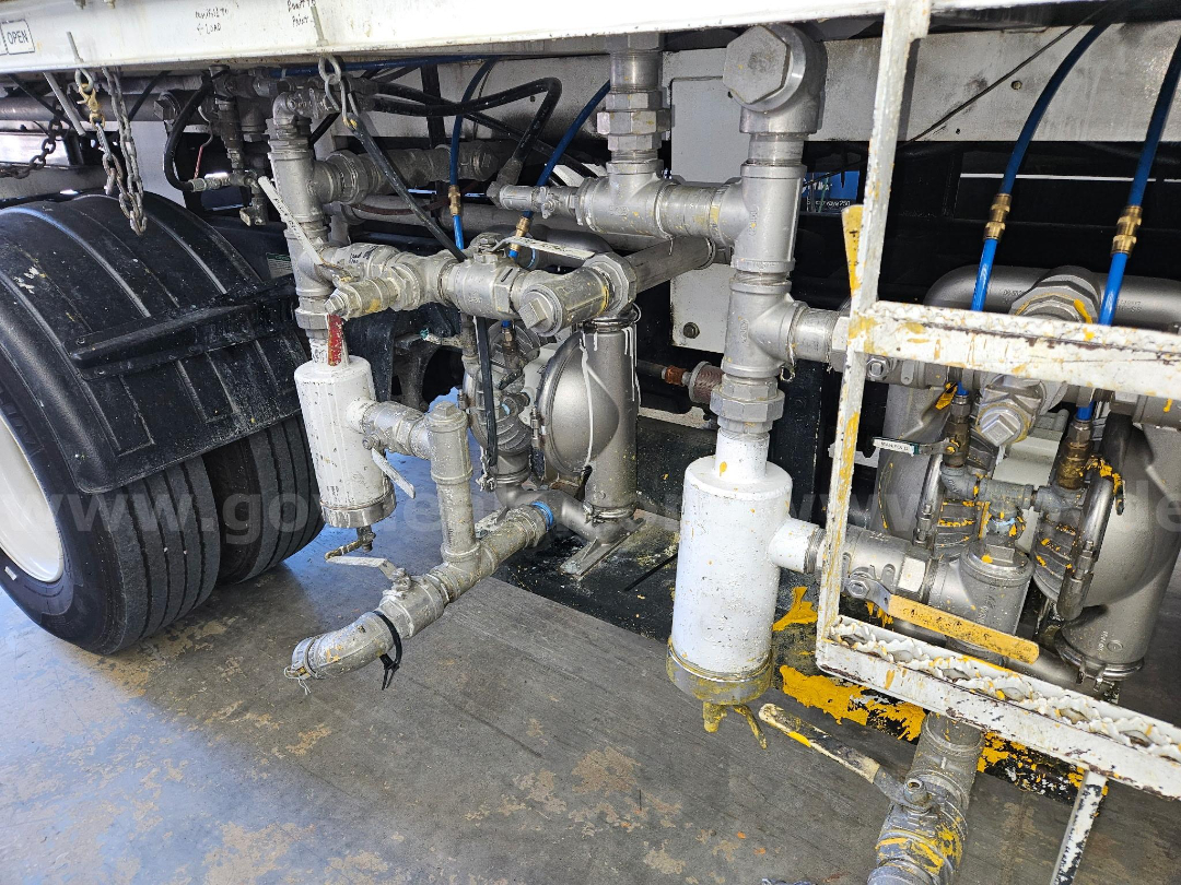 Truck undercarriage with plumbing, valves, and filter housings; multiple steel pipes, fittings, and a white cylindrical filter near the rear axle.
