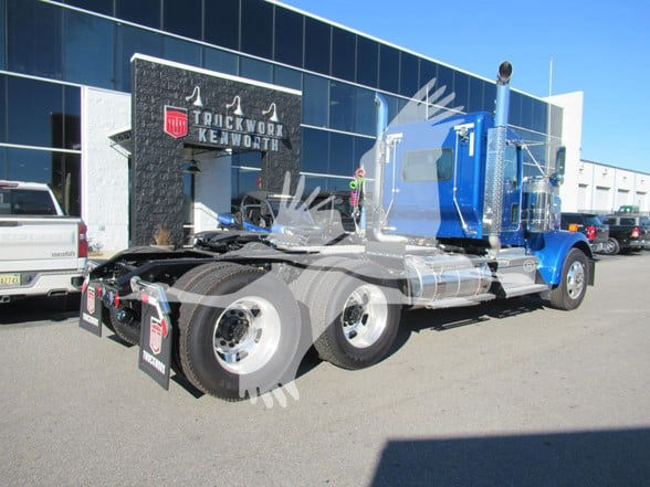 Kenworth W900L tractor truck in blue with chrome fuel tanks, front side view at dealership lot.