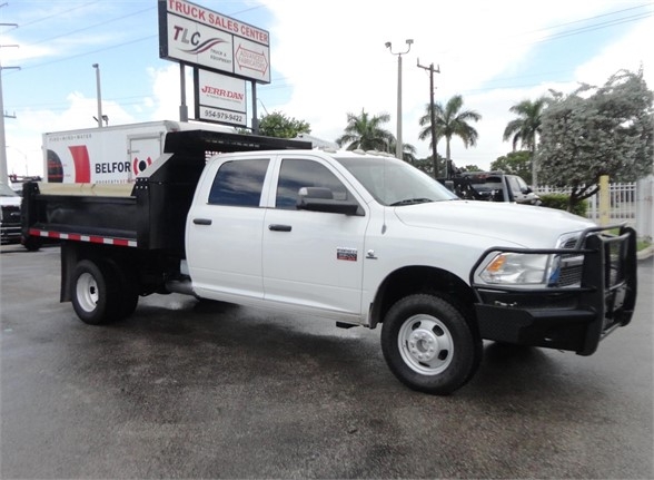 Ram 3500 dump truck side view with white cab and black dump bed, front grille guard, dual rear wheels, fleet lot background