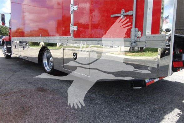 Trucking trailer rear view with red cargo box and chrome lower panel. Visible text includes no clear legible labels on the side panel; front wheel and tow hitch area are visible.