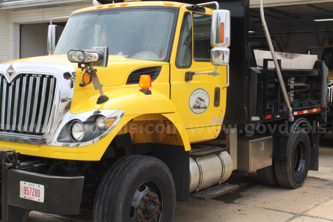 World blue and yellow International 7400 plow truck side view showing front grille, headlamps, side mirror, and plow bed with black dump box.