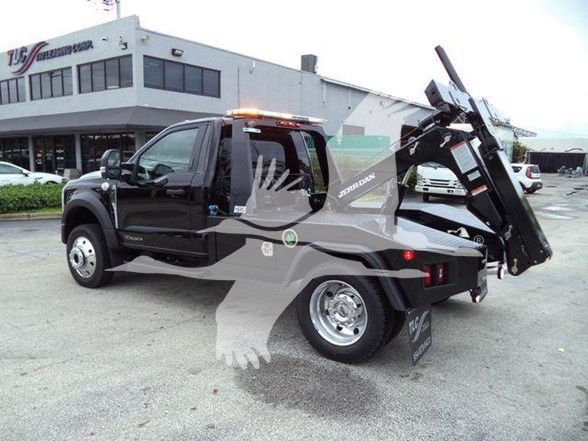 2024 Ford F450 tow truck rear dump bed with hydraulic arm and wheel lift, black body, side decals, orange beacon on cab roof.