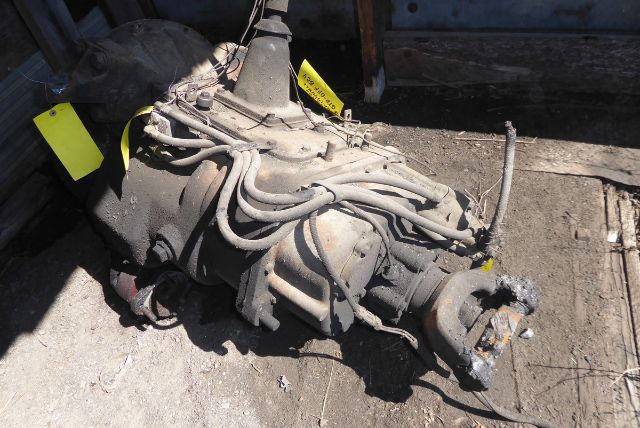 Truck transmission hanging on a concrete surface with cables and a yoke visible; yellow tags attached.