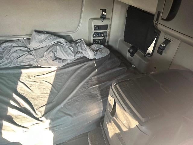Interior sleeper cab of a truck showing a bed with a blanket, storage console, and control panel with switches.