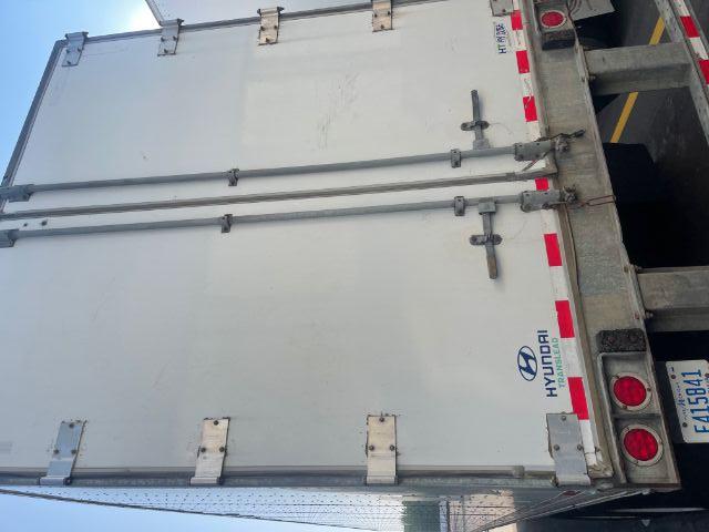 Back of a Hyundai Translead trailer with dual rear doors. Hyundai logo and 'TRANSLEAD' text visible on lower left door. Reflective red and white stripes along lower edge. License plate visible. No other legible text.