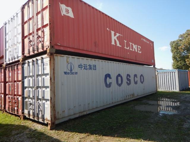 Two stacked shipping containers on a lot, red top container with K LINE branding and white COSCO container beneath.