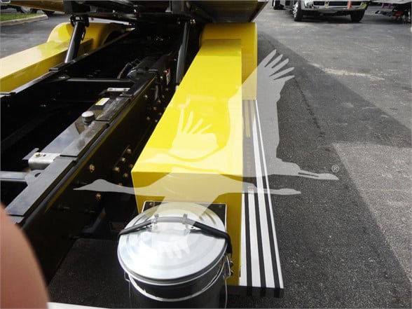 Tow truck chassis with bright yellow frame and hydraulic components, round aluminum reservoir cap, black hoses, and rails visible.