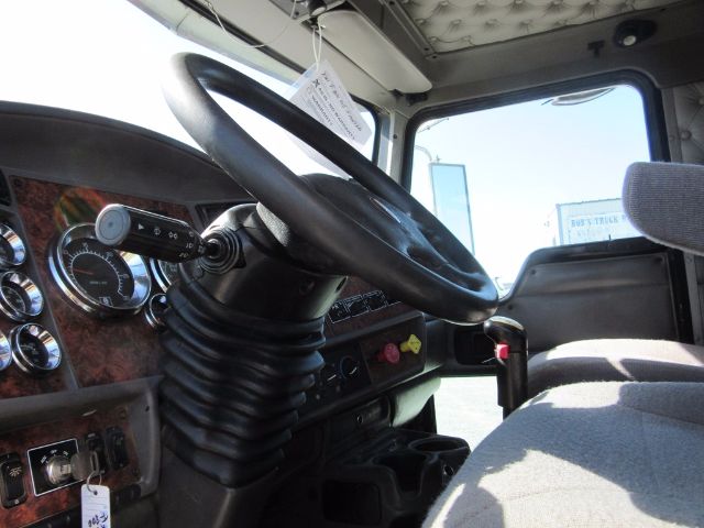 Truck interior showing steering wheel and dashboard of a 2005 Kenworth T800 daycab with textured wood paneling and gauges.