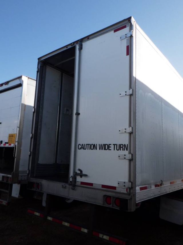 Rear view of a white Utility 4000DX composite trailer with open back door, showing text 'CAUTION WIDE TURN' on the back door.