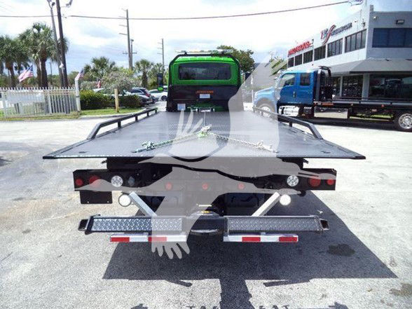 Tow truck with flatbed seen from rear, International MV, stock number J24111FM, in dealership lot.