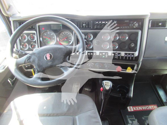 Kenworth W900L truck cabin interior with steering wheel, dashboard gauges, and manual shifter. Visible text includes 'KENWORTH' on floor mat and various gauge labels.