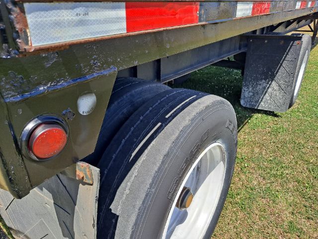 Flatbed trailer axle and dual tires with rear undercarriage showing RAM bumper and round tail light.