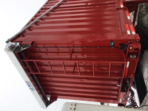 Red scrap gondola trailer with riveted steel walls, white top rail, ladder on side, and hydraulic components. Visible text includes 'Hero' on top rail.