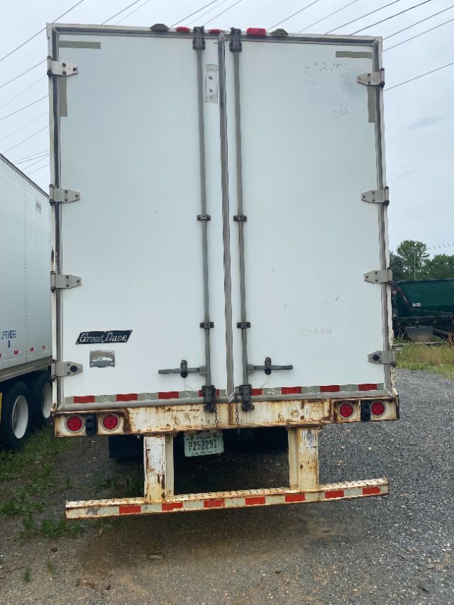 Back of a white 2015 Wabash Duraplate trailer showing double doors with vertical rails, rear underride guard, and rusted bumper; taillights and license plate visible.