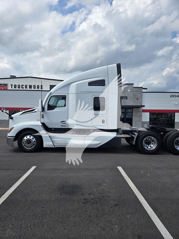 Kenworth T680 semi-truck in white, cab over engine sleeper, side view with tractor attachment, no trailer, dealership lot in background.