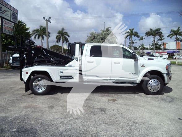 Flat side view of a white 2024 Ram 5500 Laramie pickup with a tow bed and equipment on the rear, parked on a lot.