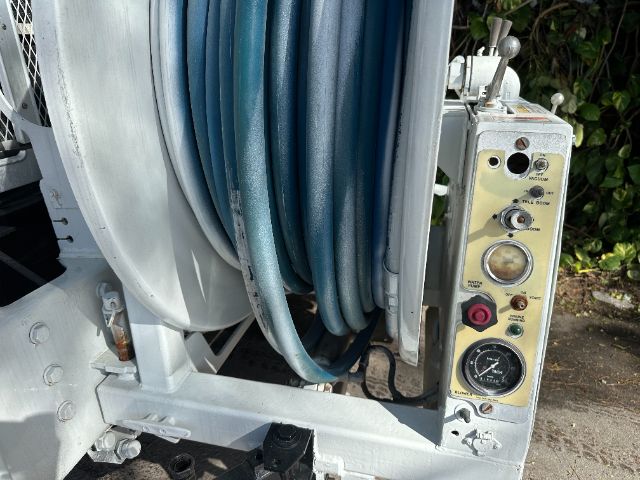 Control panel and coiled hoses on a vacuum truck reel, with gauges and switches visible on the right side.