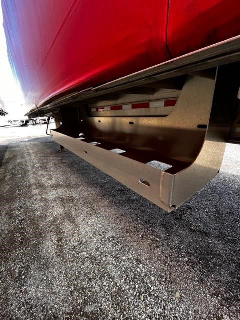 Trailer undercarriage showing a metal side rail and rolled tarp edge along the underside of a red flatbed trailer.