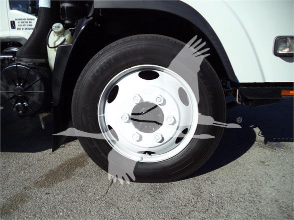 Isuzu NRR front wheel and tire assembly with silver wheel cover and black tire, part of a dump truck.