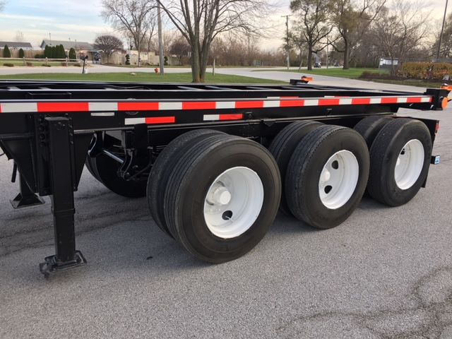 Trailer showing triple-axle chassis with black frame and white wheels, painted reflective red/white stripes along side.