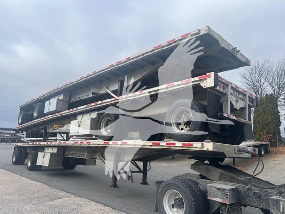 Flatbed trailer stacked on a trailer with a watermark of a bird logo overlaying the image.