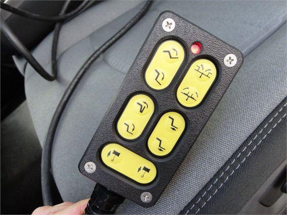Remote control with yellow buttons on a gray vehicle seat, featuring six yellow buttons and one red indicator light.