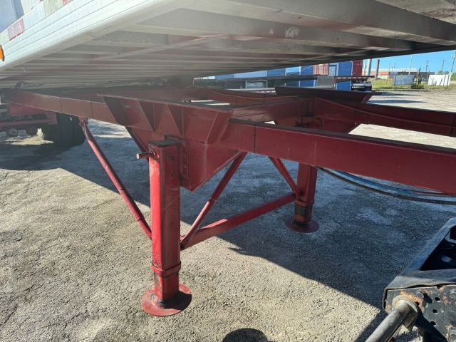 Trailer frame with red support legs and underside of a frameless GMC dump trailer.