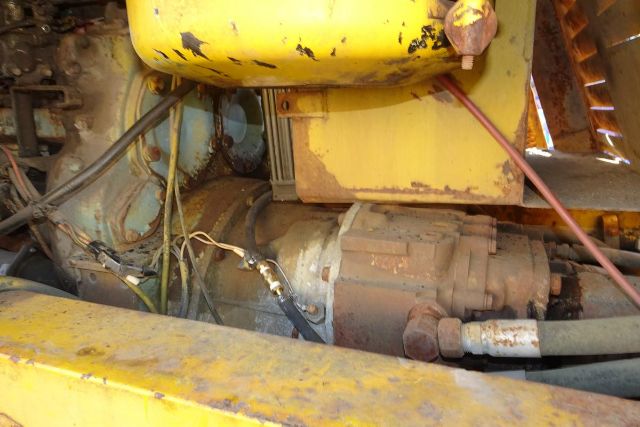 Close-up of a yellow Grove RT58 crane drivetrain showing a rusted motor, hydraulic hoses, and wiring inside a weathered truck chassis.
