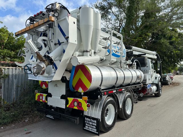 Concrete/metallic white vacuum truck with large cylindrical tank and rear-mounted equipment, rear view showing chevron warning panels and multiple hoses.