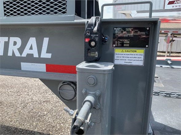 Container trailer hitch area showing a gray hand brake lever with labels, a caution sticker, and metal framework. The word 'CENTRAL' partly visible on the trailer side and a grey hitch/kingpin assembly with a black control handle and a smal