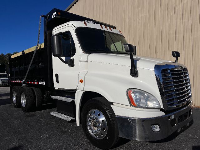 White Freightliner Cascadia 125 dump truck in driveway showing front grille and side cab with black dump bed.