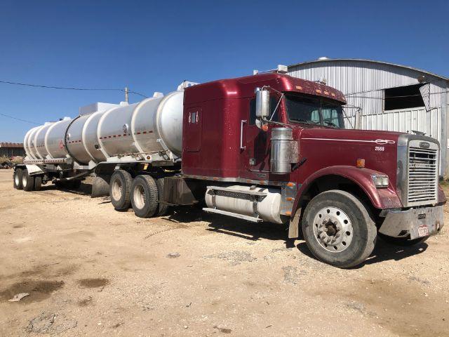 Semi truck with maroon cab and long cylindrical tanker trailer in an open lot.