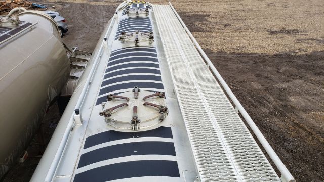 Trailer top view showing circular hatch and black painted circular patterns on white surface with diamond plate section at right side.