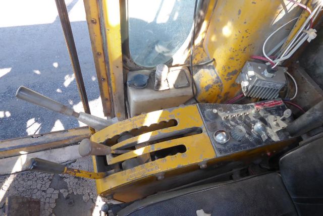 Caterpillar 16G operator cab controls with levers, yellow paint, and exposed hydraulic/ electrical components. Visible gauges and panel with switches and wiring.