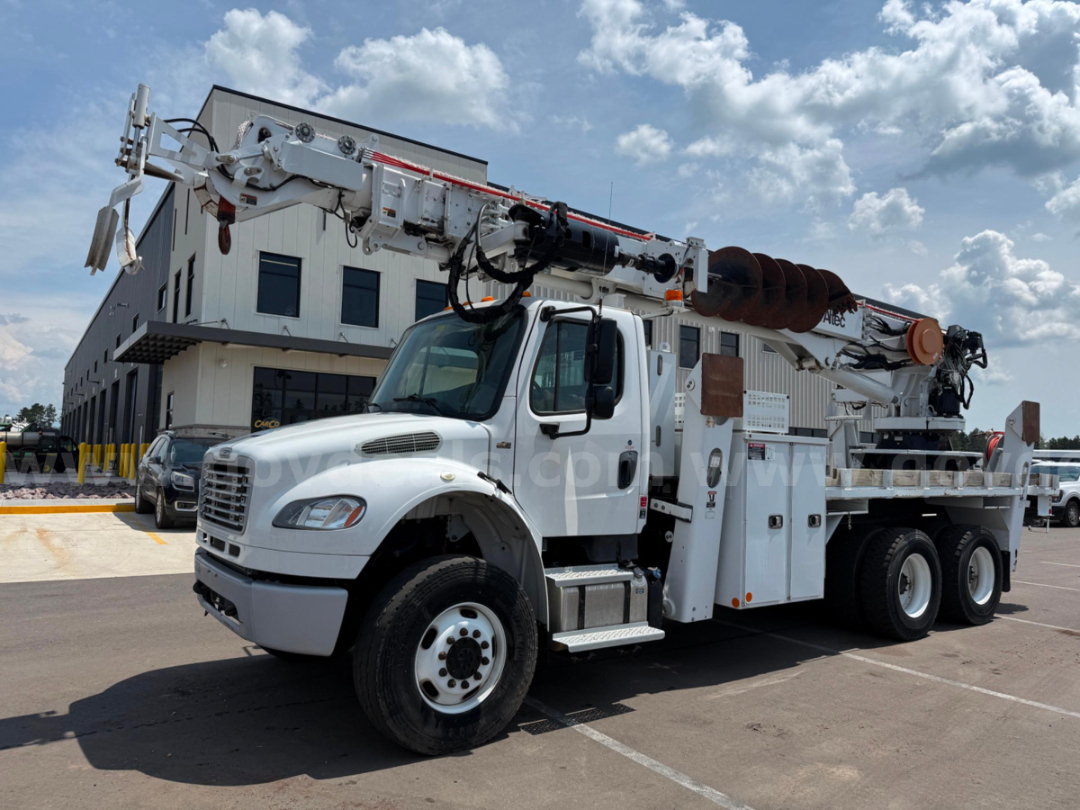 White Freightliner DT65 utility truck with large crane/boom and auger on a service lot.