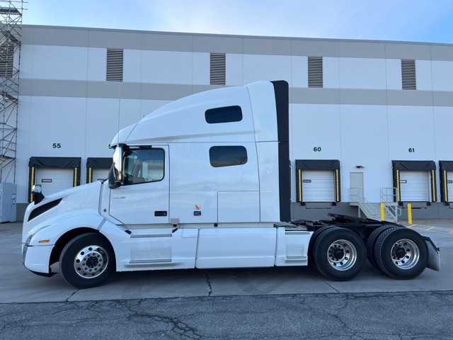 Volvo 760 conventional sleeper truck side profile with white cab and sleeper, 3-axle rear, docking bays in background.