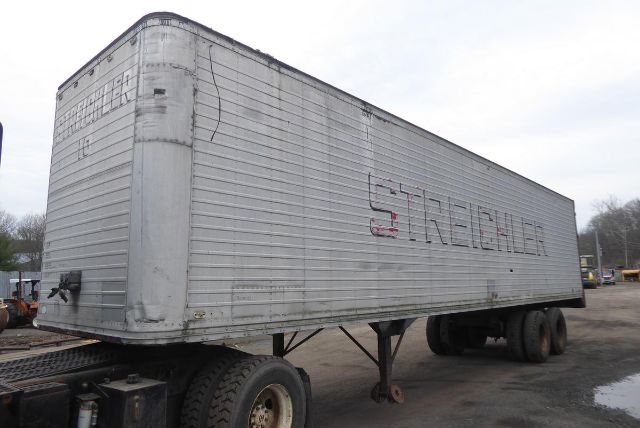 Trailer with metal exterior and faded lettering showing 'STRECK' or similar on the side, twin rear axles, elevated hitch area, overcast yard.