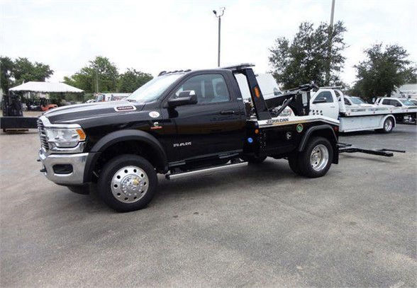 2024 Ram 4500 SLT tow truck with flatbed, black crew cab, chrome front grille, dual rear wheels, RAM badge on fender, and towing equipment on bed.