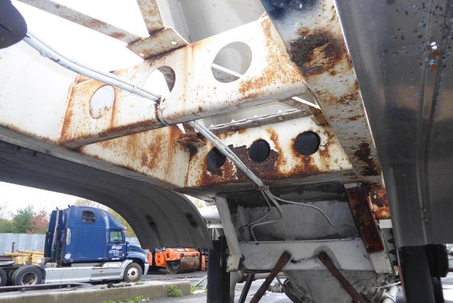 Pneumatic dry bulk trailer undercarriage with rusted steel frame and support components, wheel well, and hoses visible.