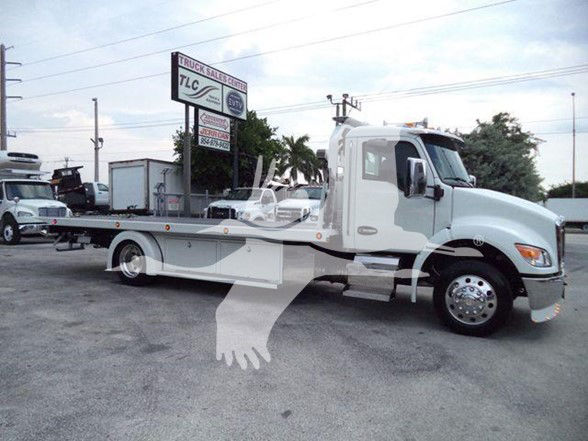 Kenworth T270/T280 tow truck with a flatbed, white exterior, side mirrors, and dual rear wheels. Visible stickers and signage in the background, including a TLC sign.