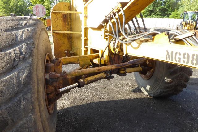 Wheel and front axle of a Caterpillar 16G motor grader with hydraulic lines and suspension components visible.