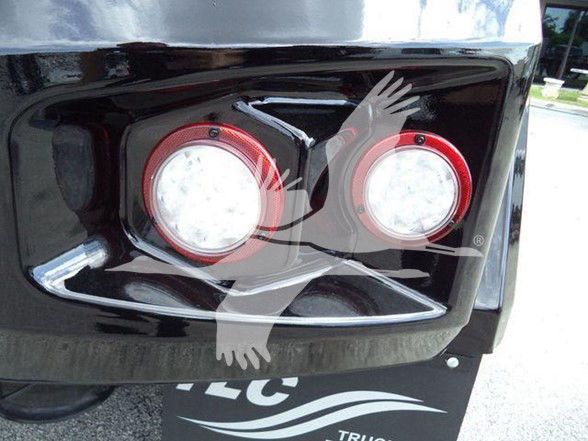 Tow truck rear showing circular taillights and glossy black bumper panel.
