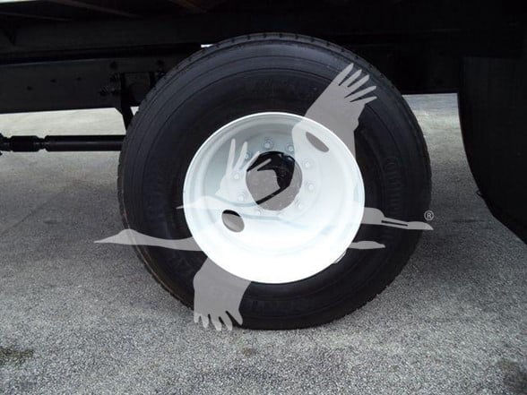 Wheel and tire on a box truck chassis with white steel rim and black tire, partial undercarriage visible.